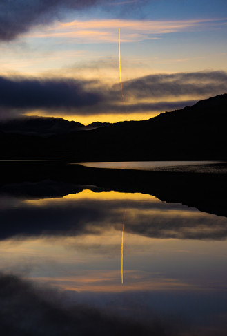 Vapour trail reflected in a still loch.